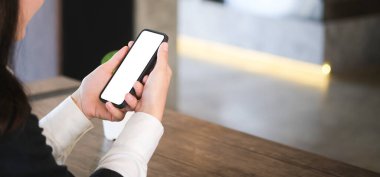 Genç kadın ellerinin çalışma odasındaki beyaz ekranlı akıllı telefonu taklit edişinin yakın görüntüsü..