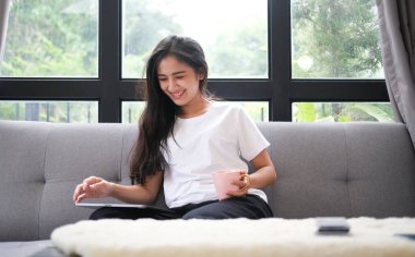 Smiling young woman freelancer sitting on sofa and working with digital tablet.	