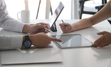 Kağıt belgelerinin istatistiklerini kontrol eden ve ofis masasındaki tablet bilgisayarda çalışan ofis çalışanlarının kırpılmış görüntüleri..