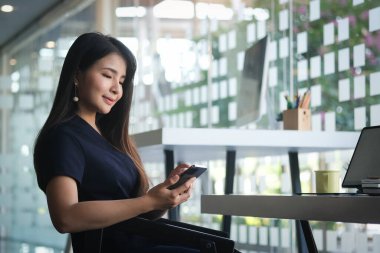 Side view of businesswoman using smartphone browsing and messaging with friends.	