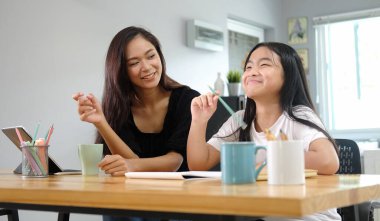 Asyalı anne, evde kızına dijital tabletle ödev yapmasına yardım ediyor..