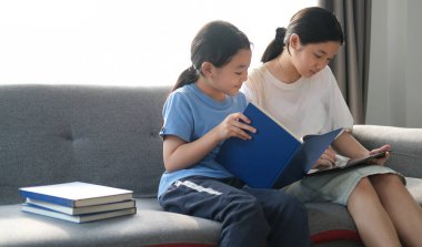 Two young asian girls sitting on sofa and using digital tablet together.	