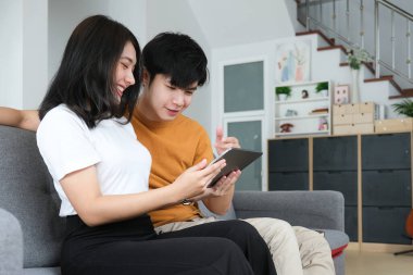 Mutlu genç çift oturma odasındaki kanepede rahatça oturuyor ve hafta sonları evdeki tablette internet gezintisi yapıyor.