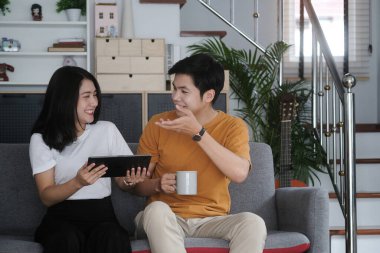 Mutlu genç çift oturma odasındaki kanepede rahatça oturuyor ve hafta sonları evdeki tablette internet gezintisi yapıyor.