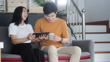 Mutlu genç çift oturma odasındaki kanepede rahatça oturuyor ve hafta sonları evdeki tablette internet gezintisi yapıyor.