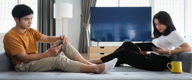 Mutlu genç çift oturma odasındaki kanepede rahatça oturuyor ve hafta sonları evdeki tablette internet gezintisi yapıyor.