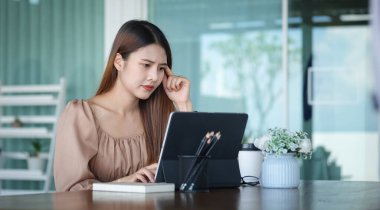 Business woman reading information on paperwork and using laptop working on desk.	