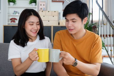 Genç Asyalı çift oturma odasında oturup birlikte kahve içiyorlar..