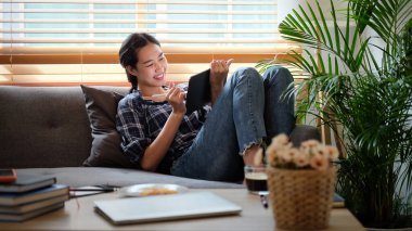 Kanepede oturup dijital tabletle çalışan gülümseyen genç kadın..