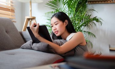 Oturma odasında otururken dijital tablet kullanan Asyalı kız.