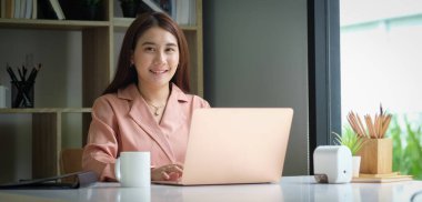 Portrait of happy young woman working on tablet pc while sitting at her working place in office.	