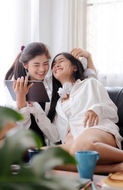 Kanepede oturup dijital tablet kullanan iki mutlu genç kadın. LGBT kavramı.