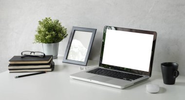 Laptop bilgisayar, kahve fincanı, ev bitkisi ve kitaplarla rahat çalışma alanı.
