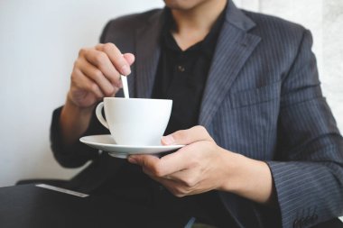 Kırpılmış iş adamı elinde bir fincan kahveyle ofiste oturuyor..