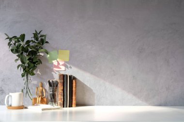 Kitaplar, kahve fincanı, not defteri ve beton duvarlı beyaz masanın üzerinde saksı bitkisi. Boşluğu kopyala.