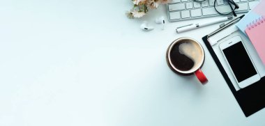 Üst düzey akıllı telefon, kahve fincanı, kalem ve defter beyaz masada. Boşluğu kopyala.