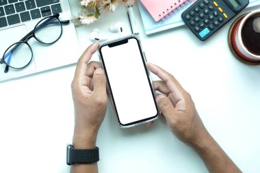 Yukarıda beyaz ofis masasında boş ekranlı cep telefonu tutan bir adam var..