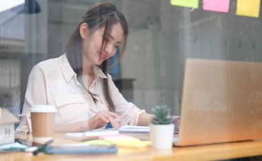 Ofis odasında dizüstü bilgisayarla çalışan gülümseyen iş kadını..
