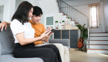 Genç çift evdeki oturma odasında dijital tablet ekrana bakarken rahat koltukta dinleniyor..