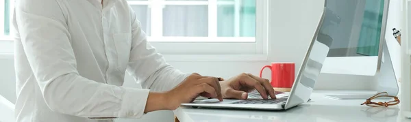 Businessman working with laptop on white table in minimal office.