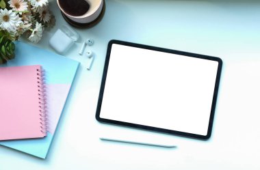 Üst görünüm dijital tablet, stilus kalem, kahve fincanı ve beyaz masadaki not defteri.