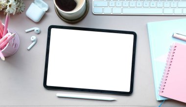 Dijital tablet, stilus kalem, kahve fincanı kulaklık ve beyaz masadaki not defteriyle kadın çalışma alanının üstünde..