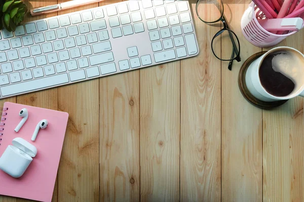 Top view female workspace with glasses, coffee cup, earphone and stationery on wooden table.