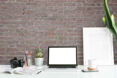 Beyaz masa üzerinde bilgisayar, ev bitkisi ve ofis malzemeleri ile yaratıcı çalışma alanı.