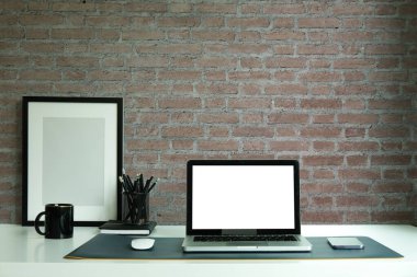 Laptop computer, digital tablet and houseplant on white table with brick wall.	