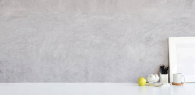 Resim çerçevesi, kulaklık, kahve fincanı ve kalem tutacağı beton duvarlı beyaz masada..