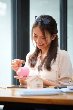 Gülümseyen Asyalı kadın gelecek için para biriktirsin diye kumbaraya para koyuyor. Tasarruf ve finansal konsept