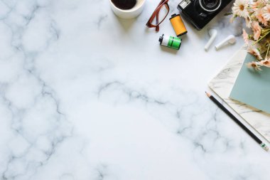 Mermer masa üzerinde kamera, bardak, kahve fincanı ve not defterleriyle yaratıcı çalışma alanı.