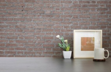 Boş fotoğraf çerçevesi, bir fincan sıcak kahve ve tuğla duvarlı ahşap masa üzerindeki bitki..