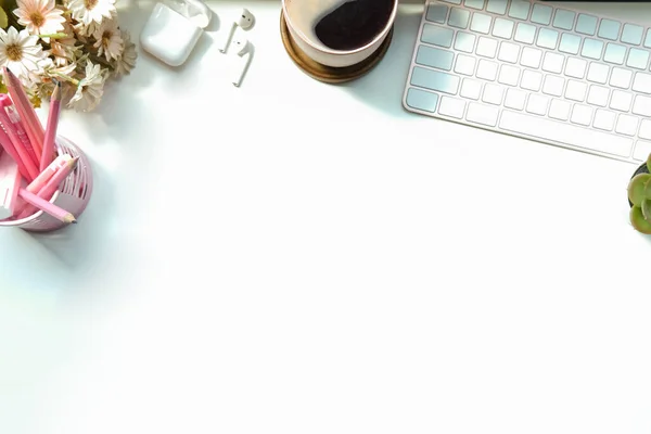 Kahve fincanı, kalem tutacağı ve klavyesi beyaz masada olan bir kadın çalışma alanı. Üst görünüm.