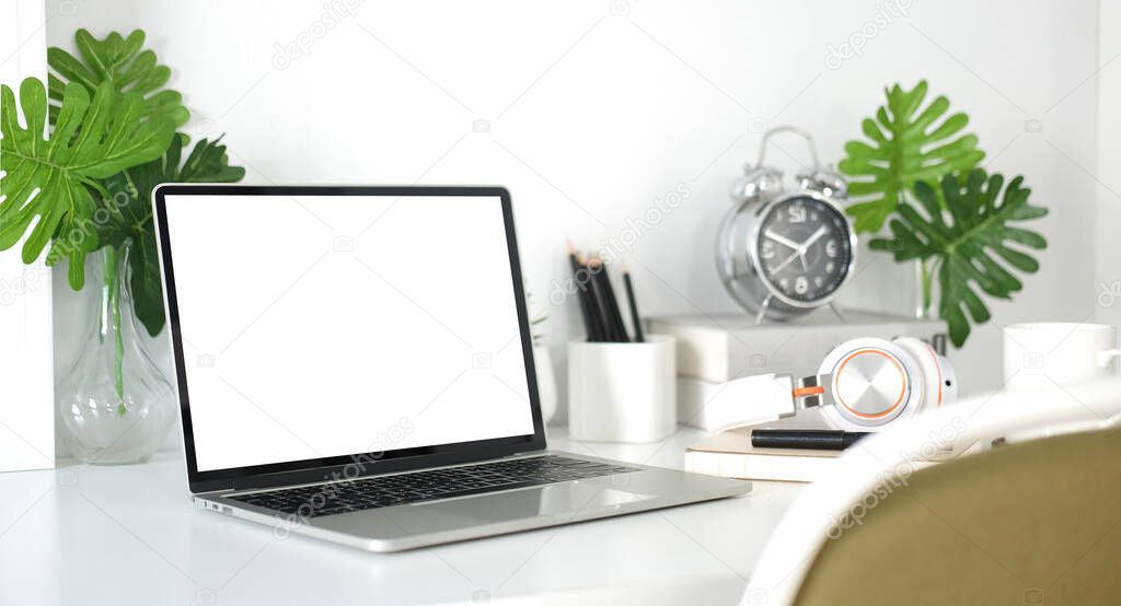 Mock up computer laptop with blank display, supplies and potted plant on white table.