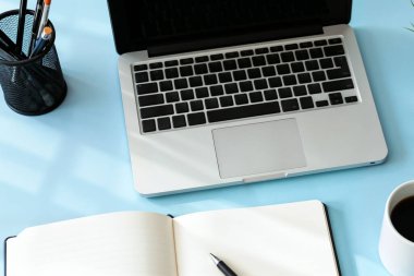 Dizüstü bilgisayarla mavi masadaki kahve ve defterleri aç