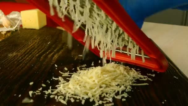 Chef hand är rivning cheddar ost för matlagning pizza, pasta eller annan maträtt på mörk skärbräda med metall rivjärn. Högen med riven ost. Hemlagad mat. — Stockvideo