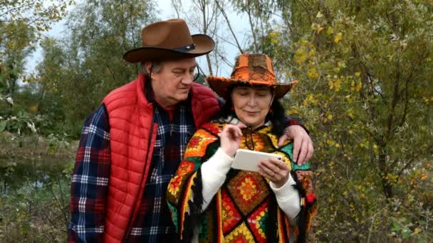 Mature adulte couple d'âge moyen famille en chapeaux de cow-boy bavarder dans un messager ou en regardant quelque chose dans leur smartphone. Dans le parc d'automne. Gros plan. — Video