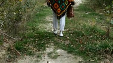 Şık, parlak giysiler içinde yetişkin bir kadının bacakları sonbaharda bir kır yolunda yürüyor. Ortam planı.