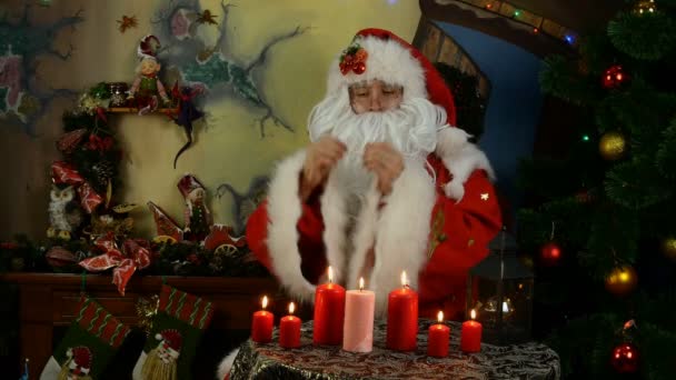 Vidám Mikulás prédikál, egyenesíti a ruháit, simogatja a szakállát a karácsonyfa mellett. — Stock videók