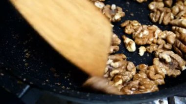 Ceviz parçaları kızarmış tavada kızartılır. Ta ki altın kahverengiye ve mutfak spatulasıyla karıştırılana kadar. Yakın plan..