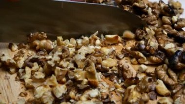 Kavrulmuş ceviz, ahşap mutfak tahtasının üzerinde mutfak bıçağıyla küçük parçalara ayrılır. Salata yapmak ya da pişirmek için..