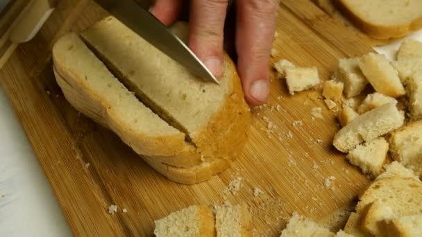 Rebanadas de pan blanco se cortan con cuchillo de cocina en cubos para hacer croutons o hardtack en tabla de cortar de madera. Cocina casera. Primer plano. — Vídeos de Stock