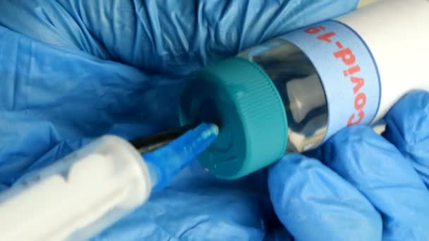 Руки медичного працівника в захисних рукавичках втягують вакцину проти коронавірусу Covid-19 у новий одноразовий шприц зі скляного флакона. Глобальна епідемія. Крупним планом . — стокове відео