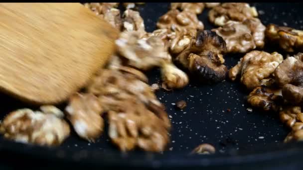 Pezzi di noci vengono fritti in padella fino a doratura e mescolati con spatola da cucina. Primo piano. — Video Stock