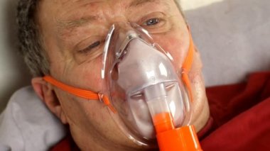 Hasta orta yaşlı adam yatakta yatarken oksijen maskesinden nefes alıyor. Astım tedavisi, alerji, bronşit, Covid-19 'da zatürree ve solunum hastalıkları. Yakın plan..