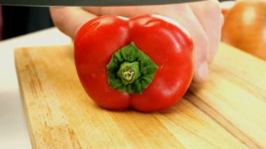 Şef salata için ahşap doğrama tahtasına büyük keskin mutfak bıçağıyla kırmızı tatlı biber kesiyor. Sağlıklı beslenme konsepti. Shakshuka tarifi. Yemek pişirme süreci. Yakın plan..
