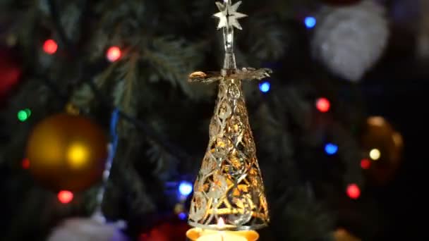 Juguete decorativo en forma de árbol de Navidad gira en círculo de la energía de la vela ardiendo debajo de ella. Sobre fondo de árbol de Navidad y guirnaldas parpadeantes. Decoraciones Año Nuevo vacaciones. — Vídeo de stock