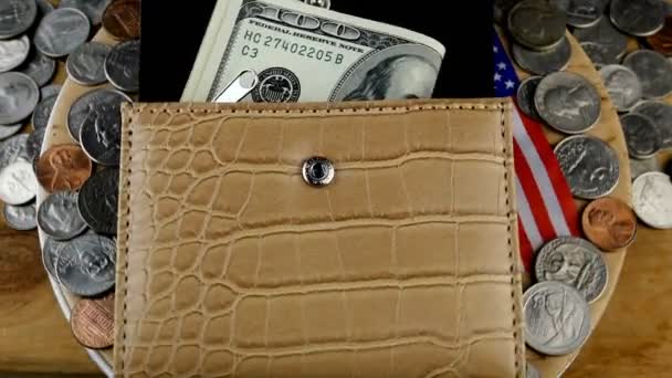 Öppen plånbok från vilken några 100 amerikanska dollar sticker ut och en hel del utspridda amerikanska cent roterar på cirkeln. Amerikansk flagga sedd från under handväskan. Närbild. — Stockvideo