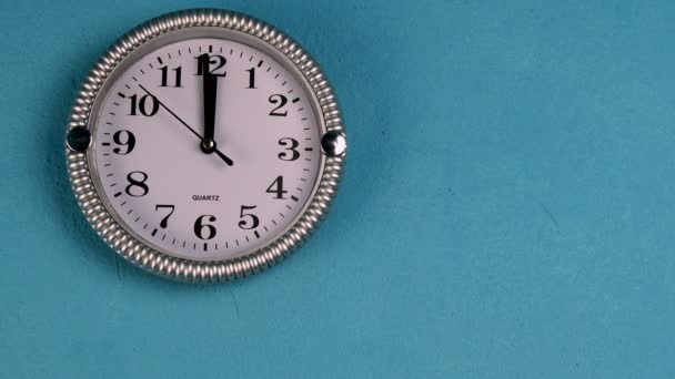 Кварцевые настенные часы с секундной стрелкой идут по часовой стрелке. Часы показывают двенадцать часов. На старой голубой стене. Средний план. — стоковое видео